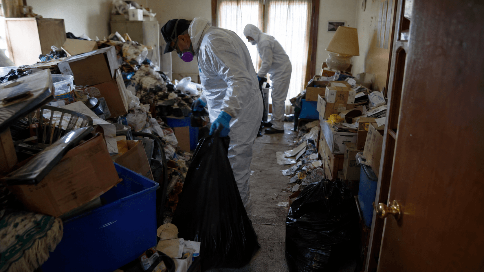 Hoarding cleanup workers using protective equipment inside a cluttered property