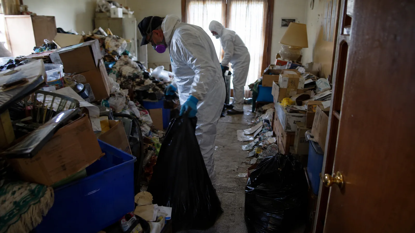 Hoarding cleanup workers using protective equipment inside a cluttered property